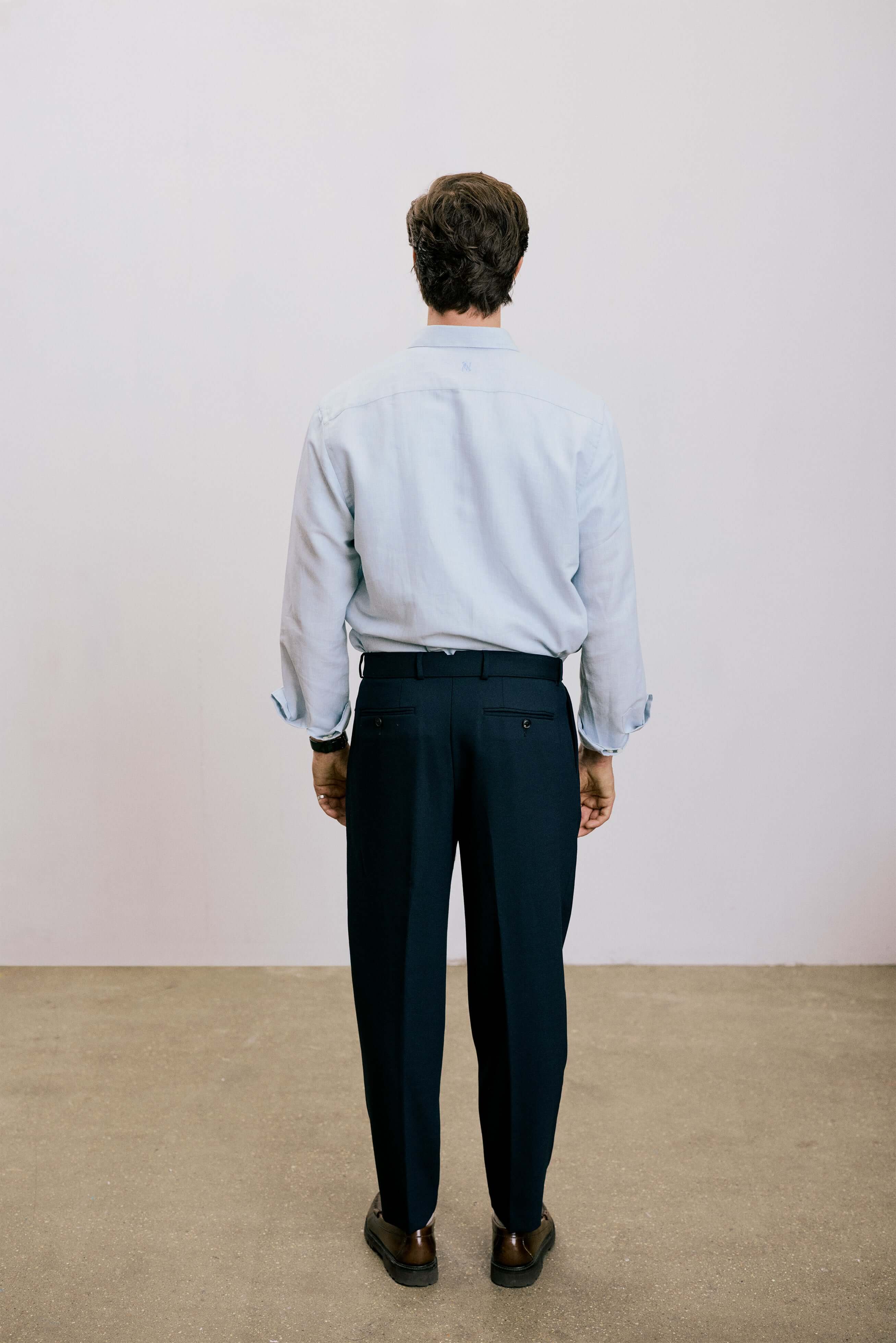Back view of a man wearing VARRO Evelyn Mist Blue shirt, showcasing relaxed fit and hidden button-down collar with dark pants.