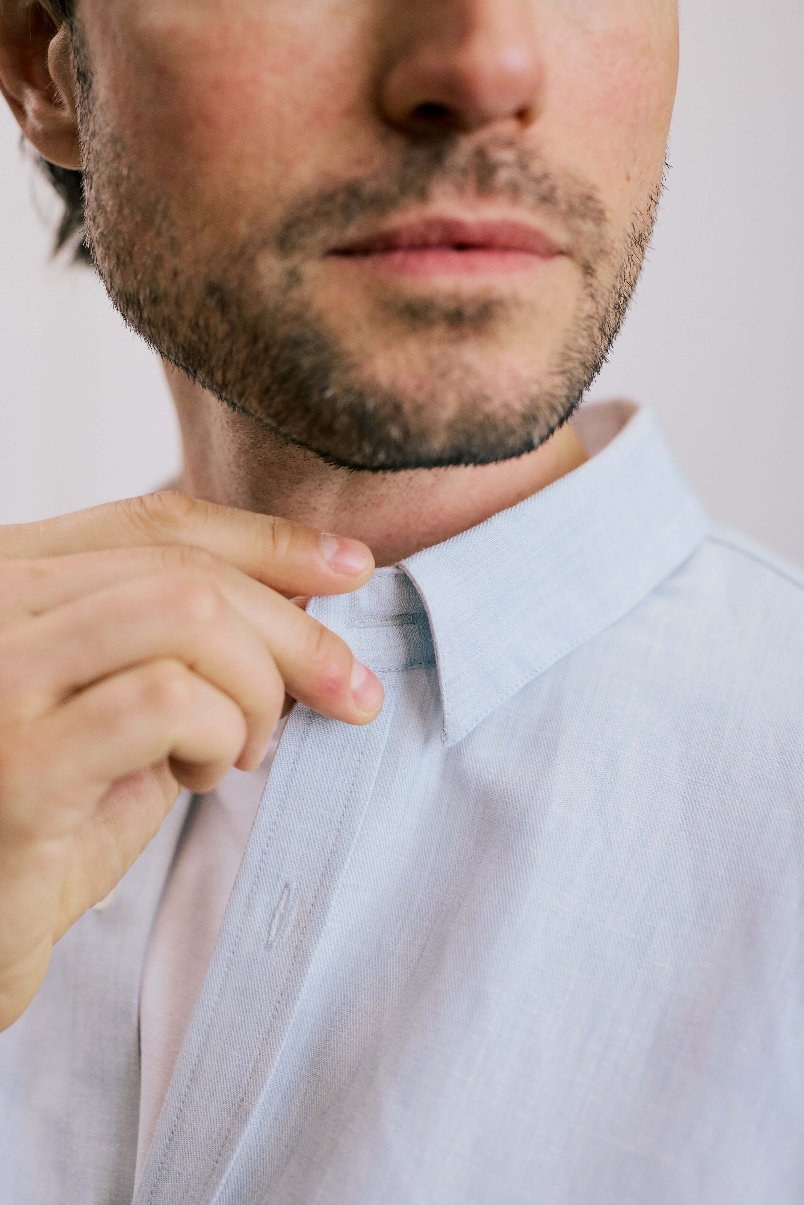 Close-up of a man adjusting the hidden button-down collar of the VARRO Evelyn Mist Blue shirt, showcasing the hemp cotton merino blend.