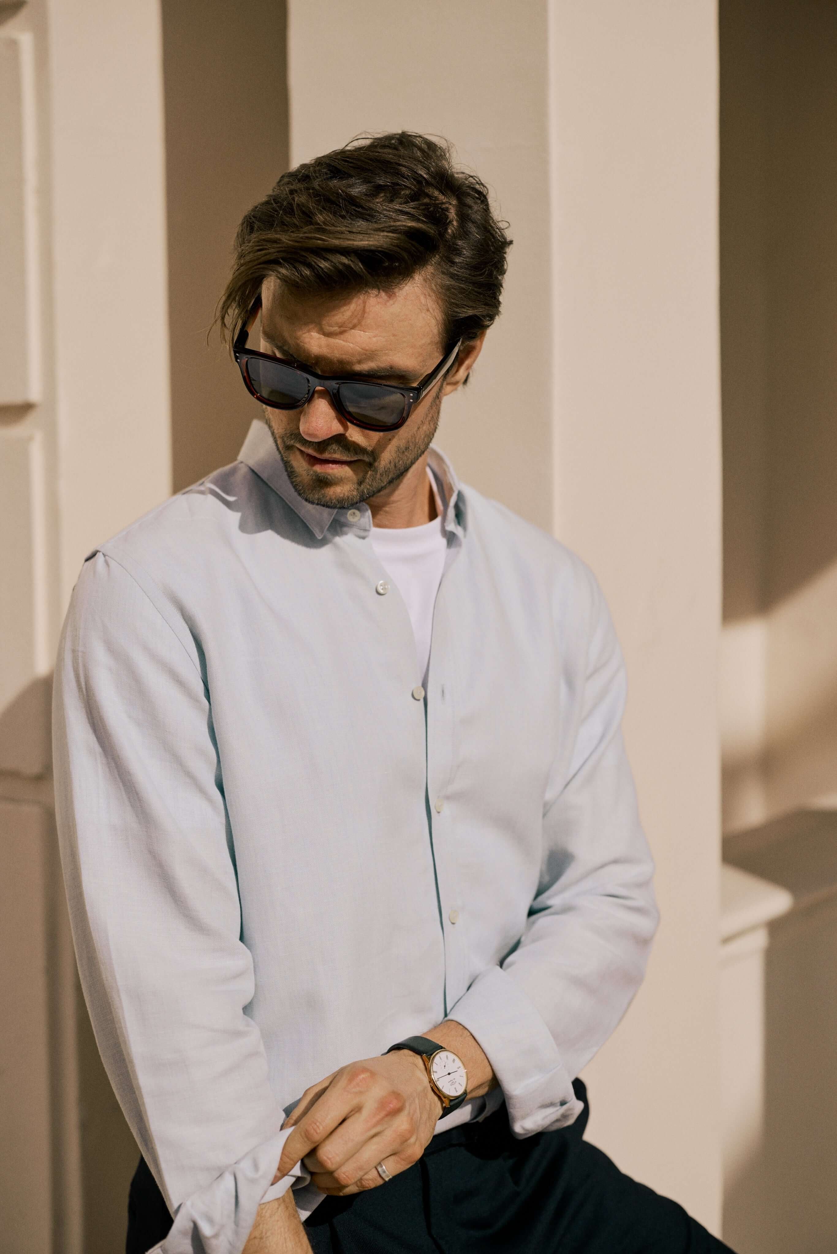 Man adjusting his cuff while wearing a VARRO Evelyn Mist Blue shirt, showcasing the relaxed fit and hidden button-down collar.